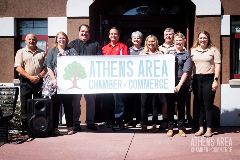 A group of people standing in front of a building holding a sign that says athens area chamber of commerce.