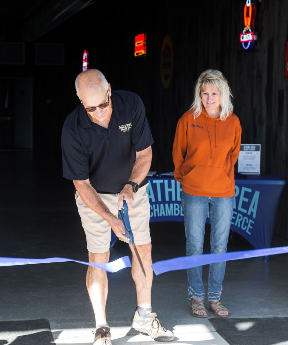 A man is cutting a blue ribbon while a woman watches