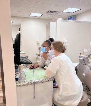Two female dental assistants are posing for a picture in a dental office.