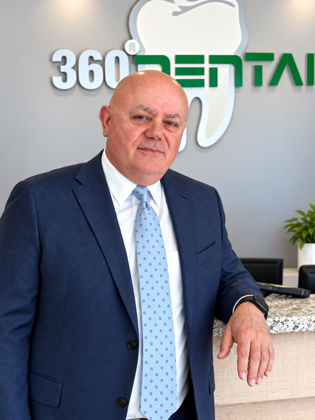 Dr. Sitkovetskiy in a navy suit leaning on a desk in a dental office with a 360 Dental sign behind him