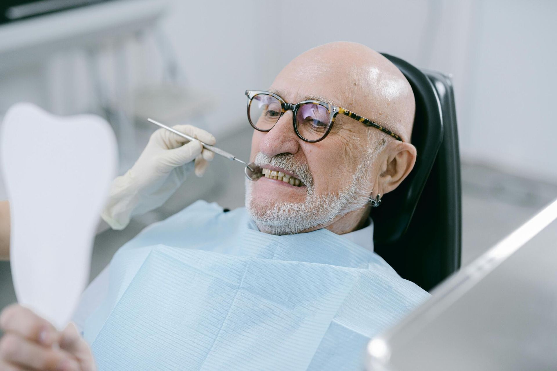 Dentist examining a smiling patient in a dental chair, with a tool near the mouth.
