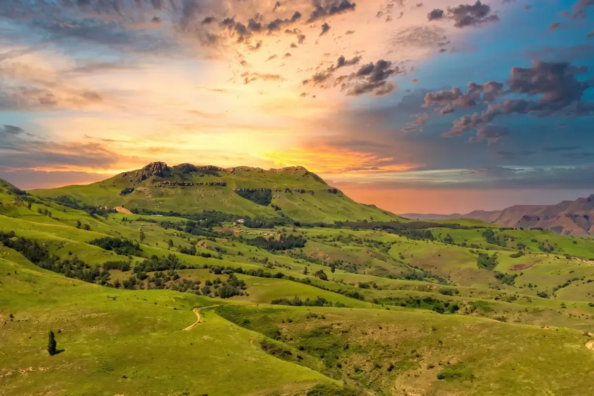 Sunset over lush green hills beneath a colorful cloudy sky