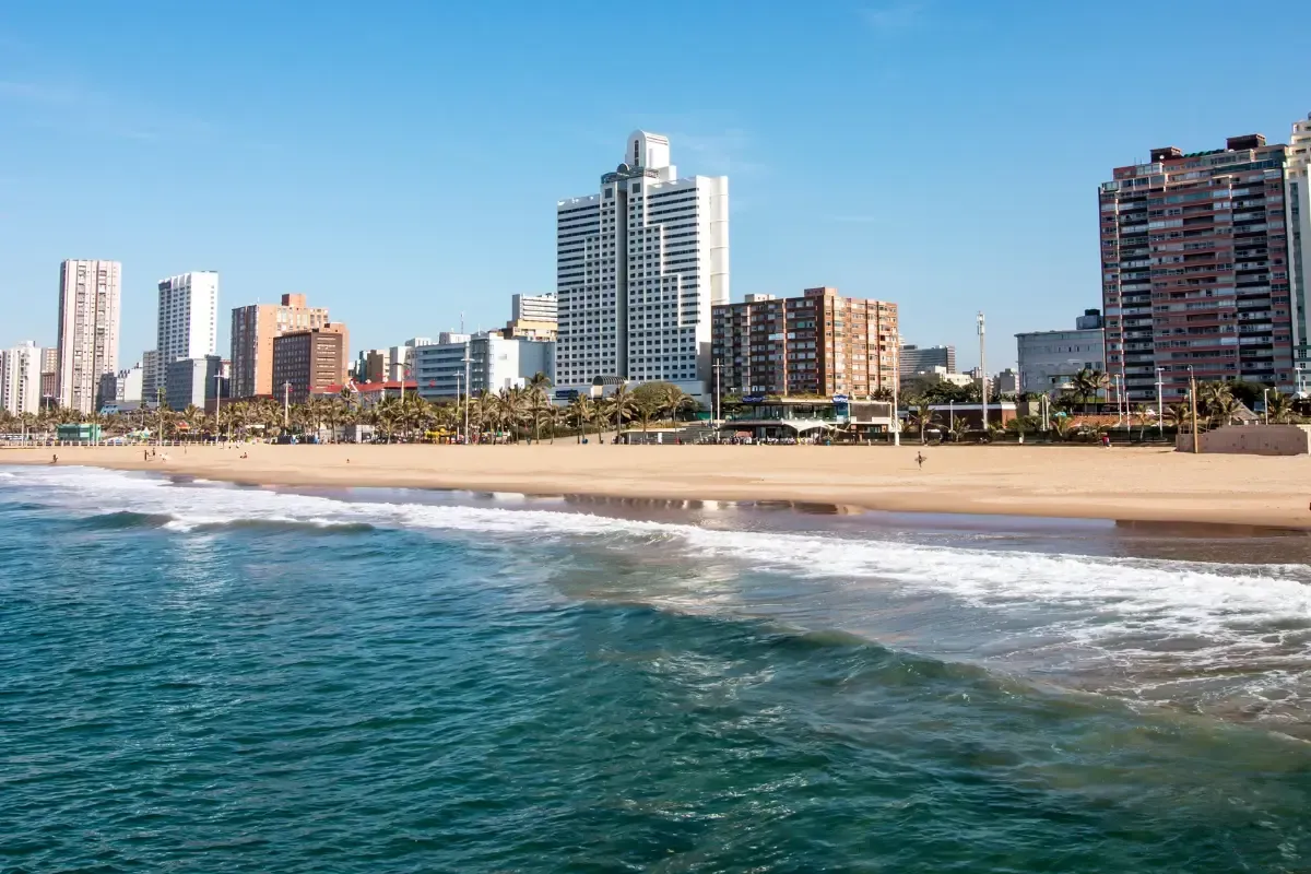 City skyline beside a sandy beach and turquoise ocean under a clear blue sky