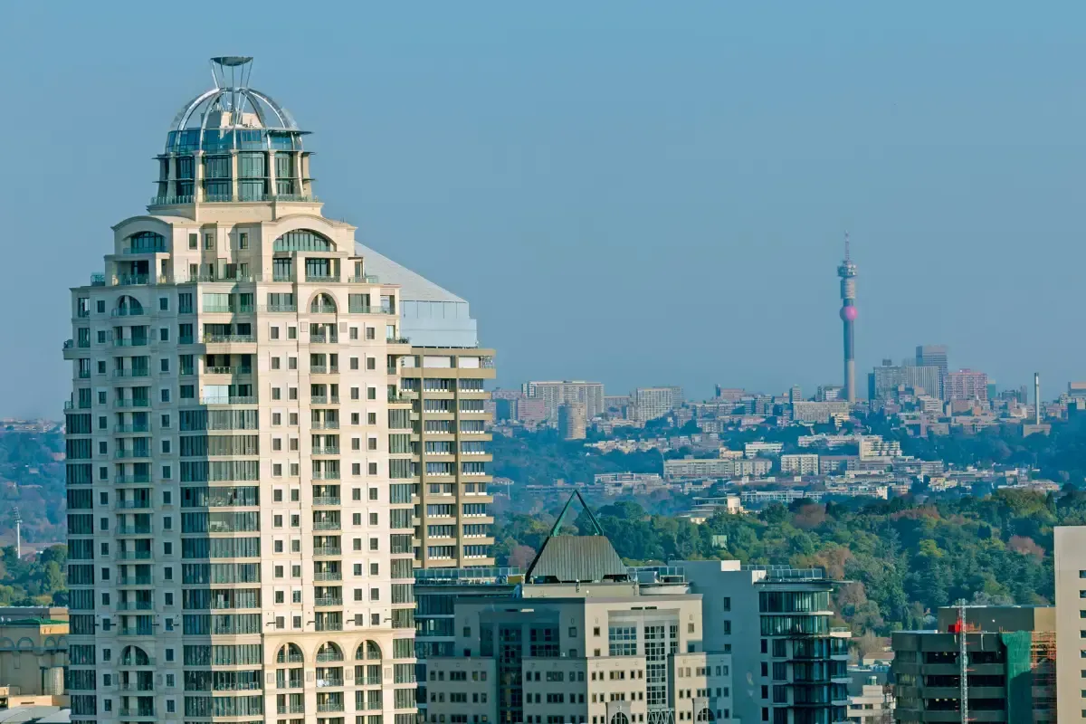 City skyline with a tall white building and a distant tower under a clear blue sky