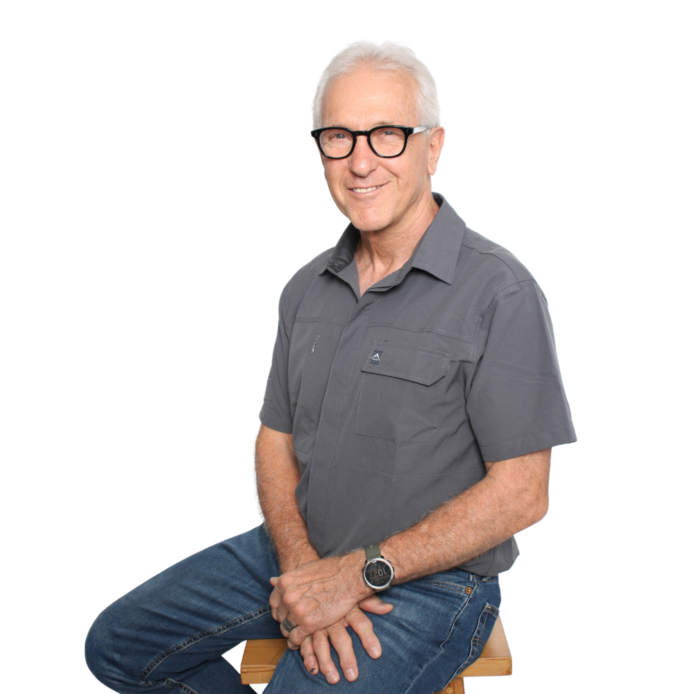 Man sitting on a stool, wearing glasses, a gray shirt, and jeans, against a white background