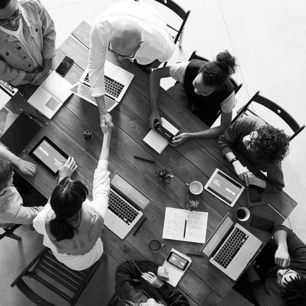 Overhead view of a team meeting around a wooden table with laptops, documents, and coffee cups