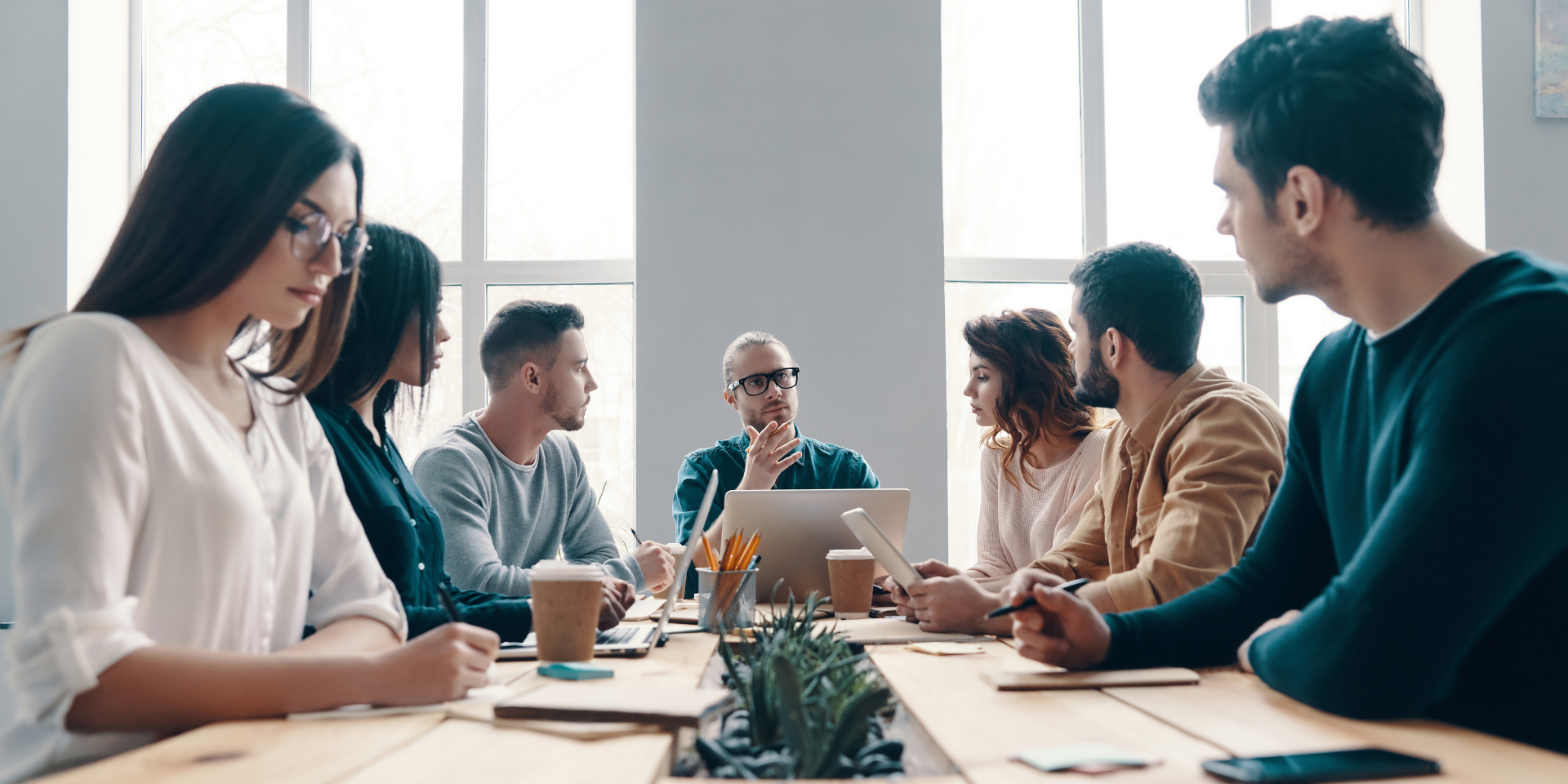People in a bright meeting room discussing over coffee and laptops around a table
