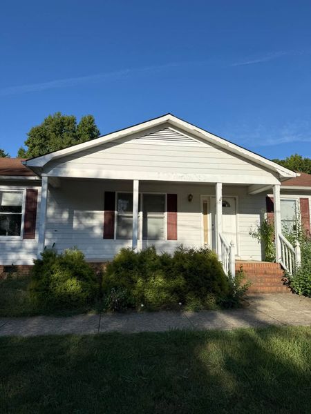Single-story white house with front porch, red door, and brick steps under a clear blue sky