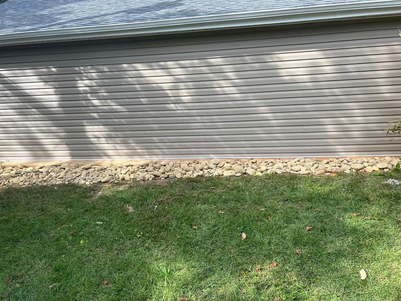 Grassy yard beside a corrugated metal fence with dappled sunlight and a narrow stone border