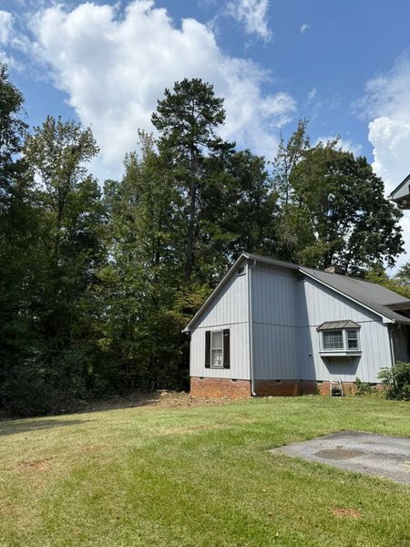 Small white shed with red brick base beside trees under a partly cloudy sky