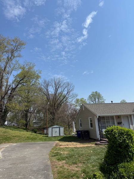 Suburban house with a curved driveway, small shed, and trees under a clear blue sky