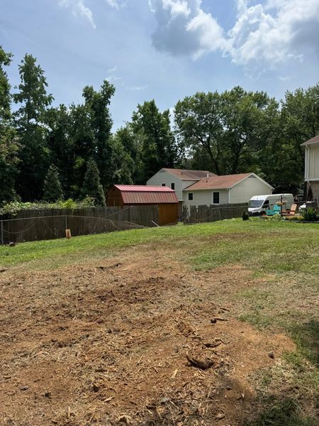 Grassy yard with dirt foreground, trees, and small houses under a bright blue sky.