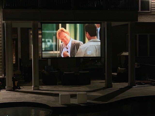 A screen shows a man in a suit talking to another man