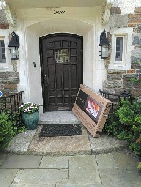 A large flat screen tv is sitting on the porch of a house.