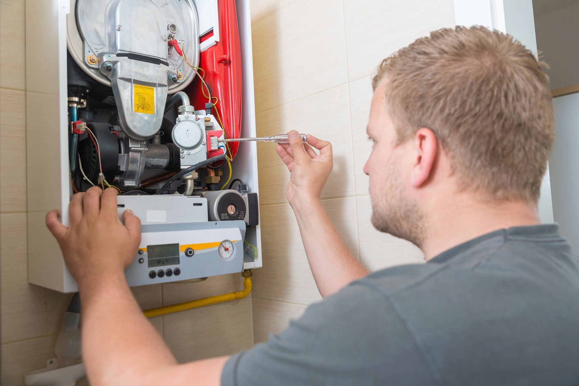 Man is Fixing a Boiler With a Screwdriver — Tucson, AZ — Orozco Brothers Plumbing Heating and Cooling