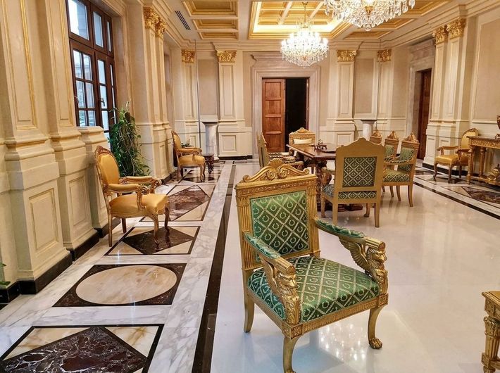 Elegante sala lounge di un hotel, con finiture dorate, poltrone imbottite verdi, lampadari e pavimenti in marmo