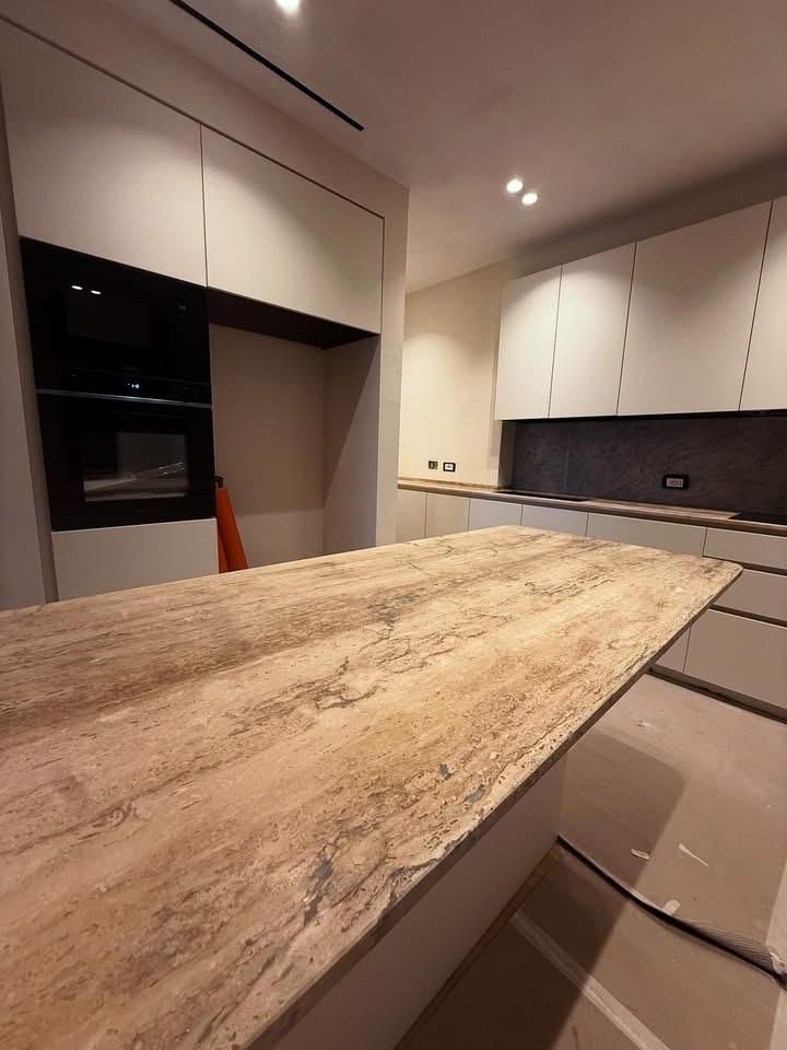 Cucina moderna con ampia isola in pietra, mobili bianchi ed elettrodomestici da incasso