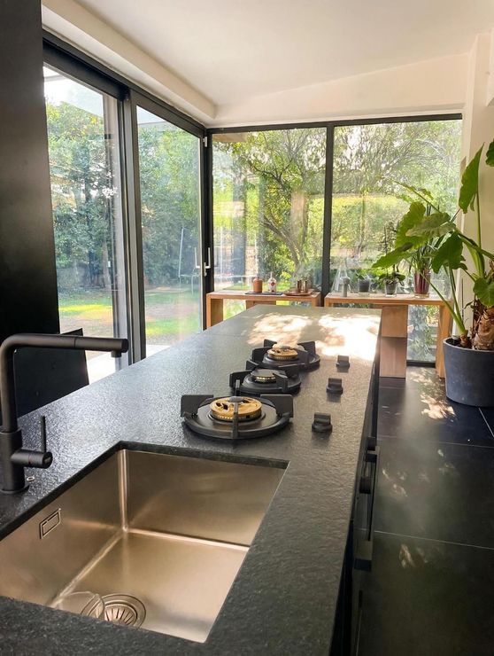 Cucina moderna e luminosa con isola nera, lavello, piano cottura e ampie finestre affacciate sul verde
