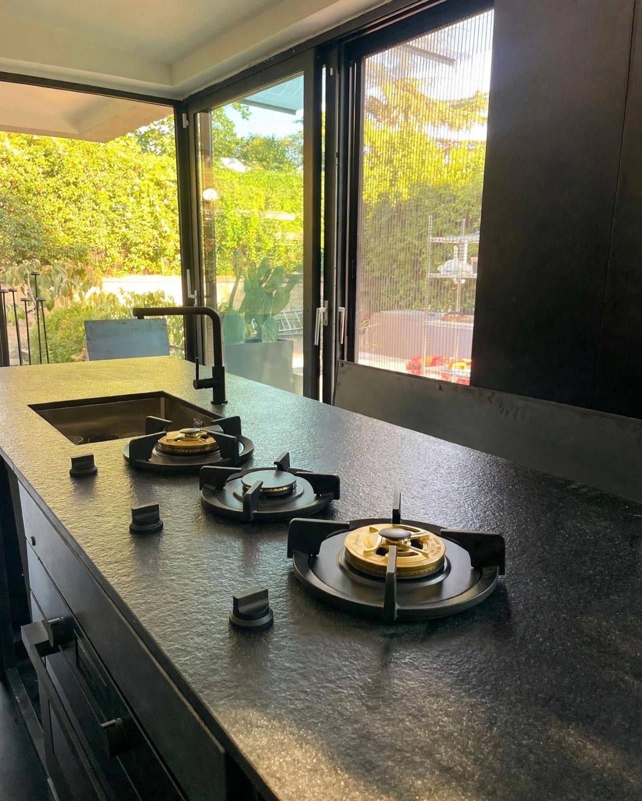 Cucina moderna con piano di lavoro nero, fornelli a gas e ampie finestre affacciate sul verde