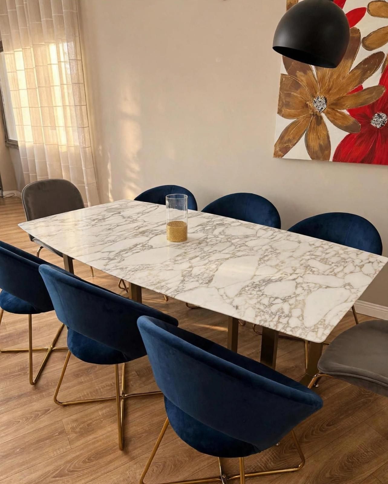 Sala da pranzo moderna con tavolo in marmo, sedie blu, pavimento in legno e decorazioni floreali alle pareti