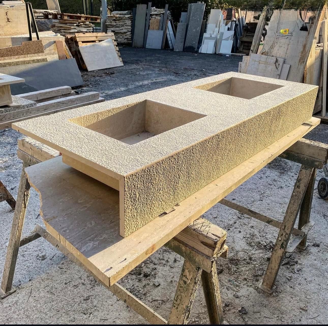 Un piano lavabo in pietra con due vasche rettangolari, appoggiato su un cavalletto di legno in un deposito di pietra.