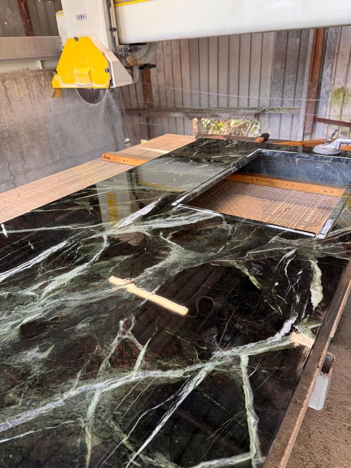 Lastra di marmo nero su un tavolo da lavoro, con un paranco giallo sospeso e piastrelle di pietra sullo sfondo