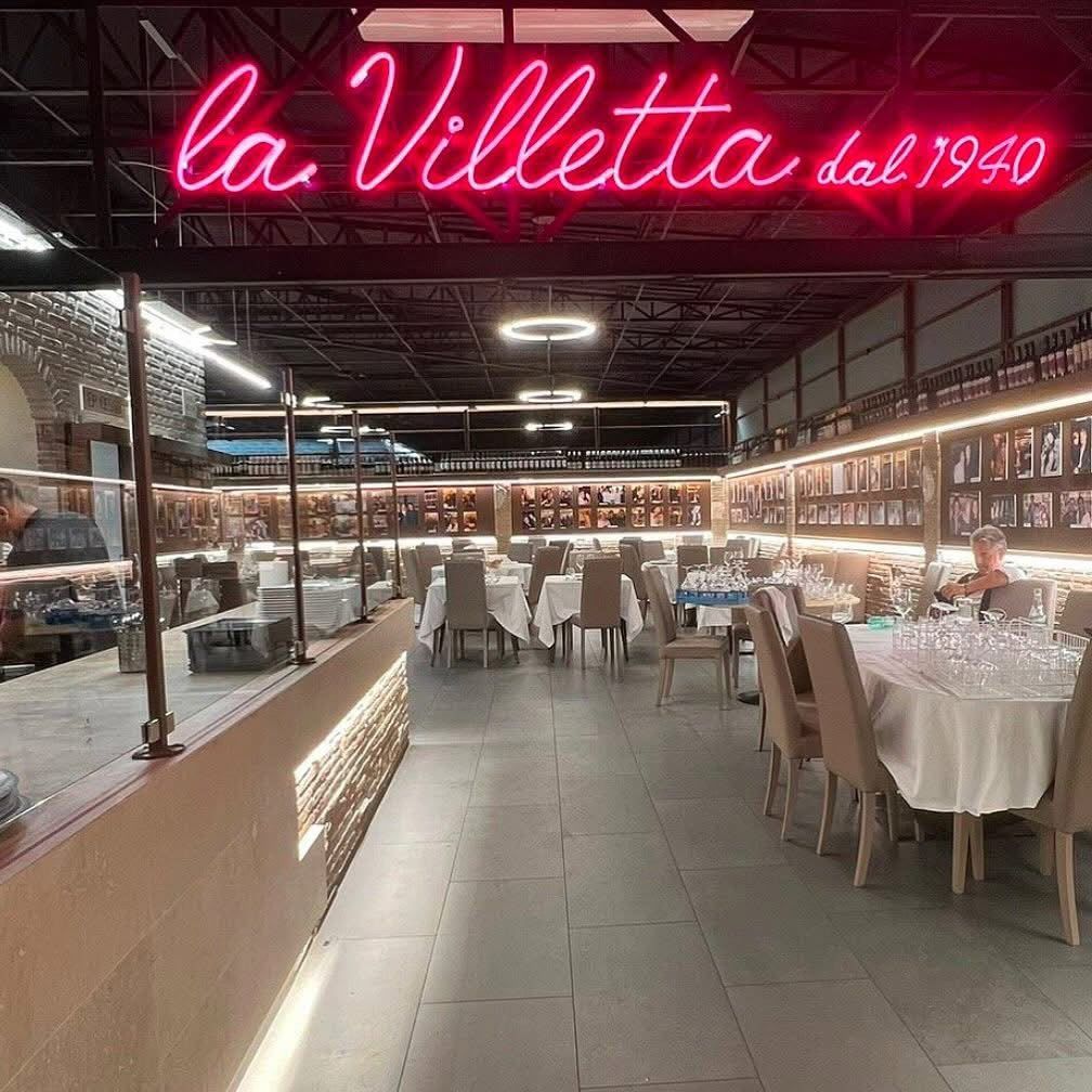 Elegante interno di ristorante italiano con l’insegna al neon «la Villetta dal 1940» e tavoli apparecchiati.