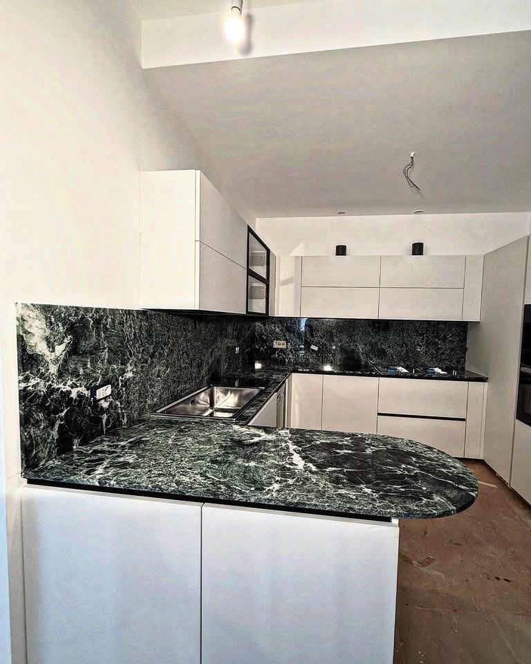 Cucina moderna con mobili bianchi e piani di lavoro e paraschizzi in marmo verde scuro, in fase di costruzione