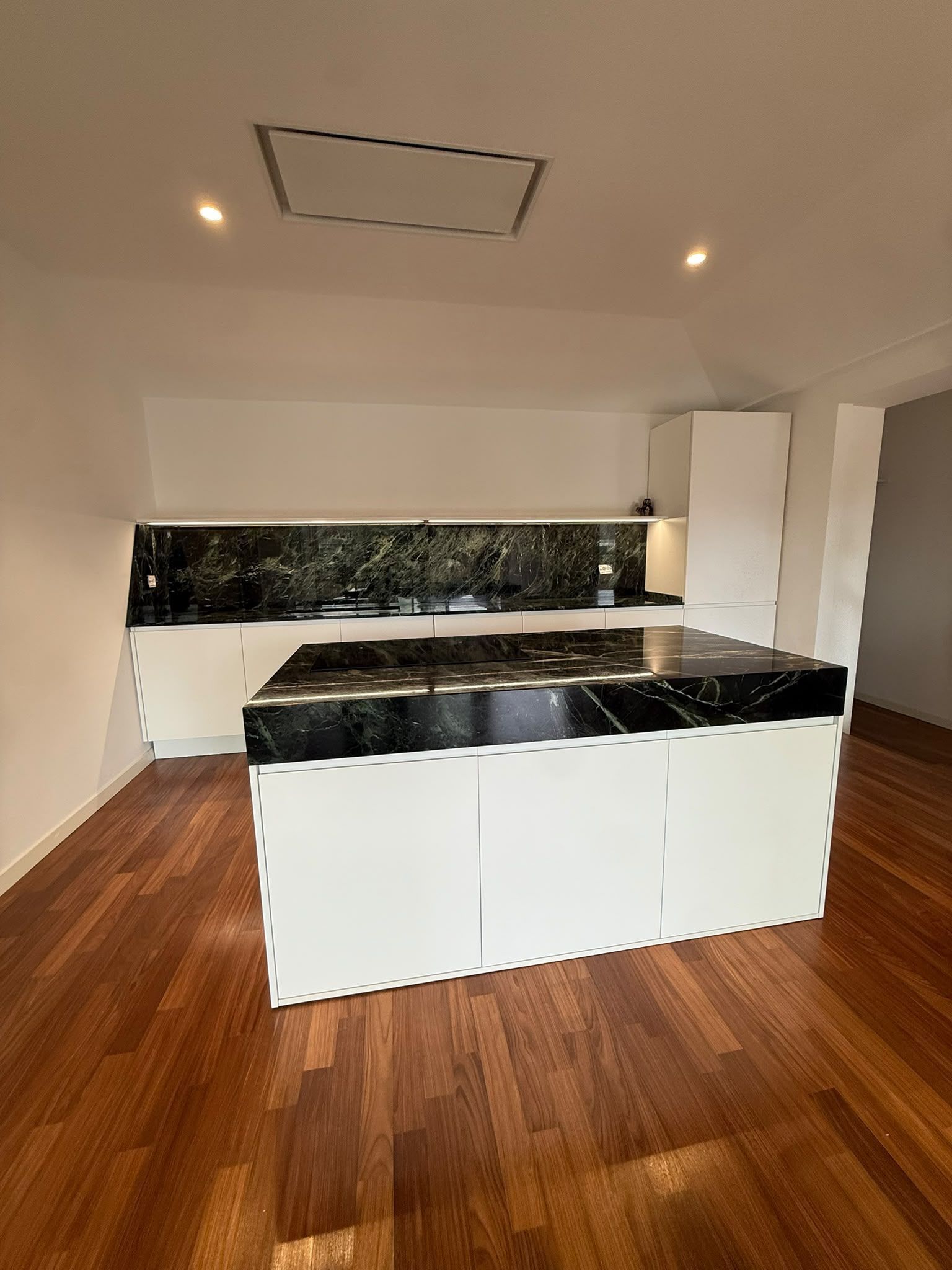 Cucina moderna con piani di lavoro neri, mobili bianchi e pavimento in legno.