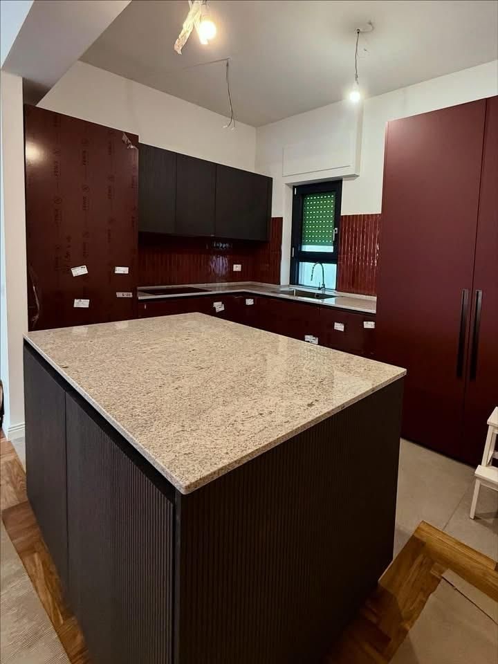 Cucina moderna con mobili in legno scuro, piano dell’isola puntinato e una finestra con tende verdi