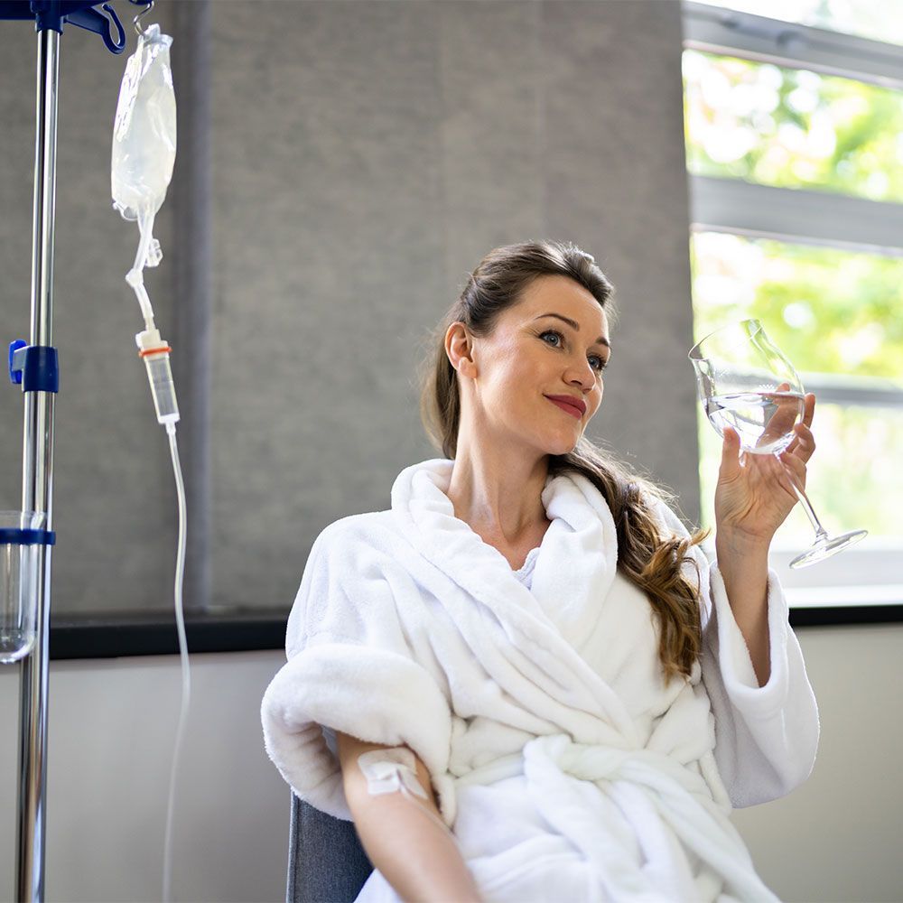 A woman in a bathrobe is holding a glass of wine in a hospital room.