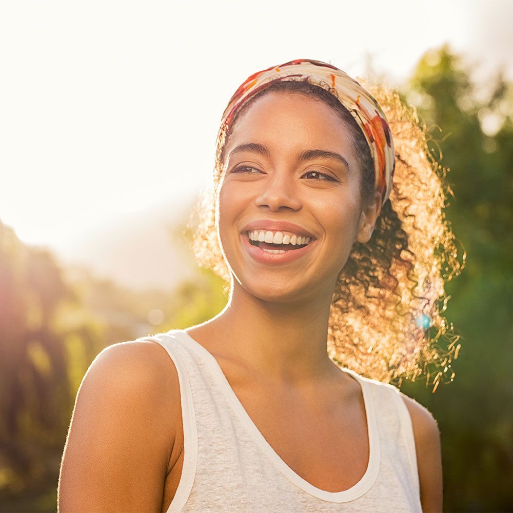 A woman wearing a headband and a white tank top is smiling.