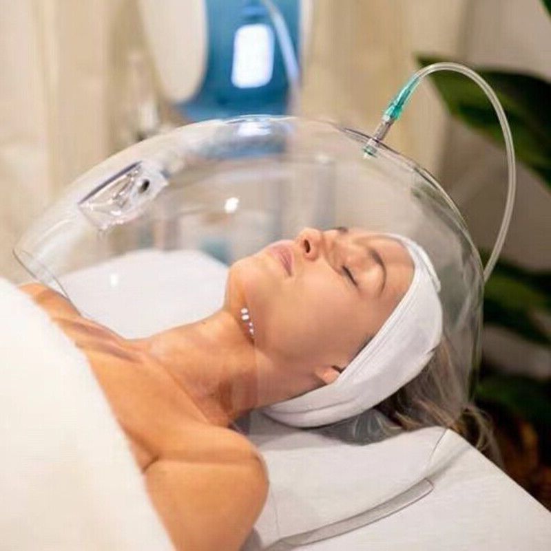 A woman is laying on a bed with a clear dome over her head.