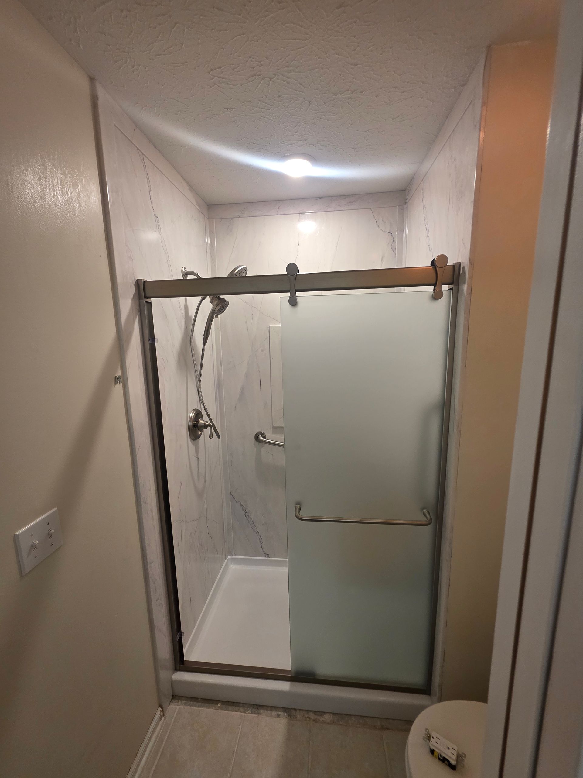 Shower stall with glass doors and marble-look walls. Includes a grab bar and shelves with toiletries.