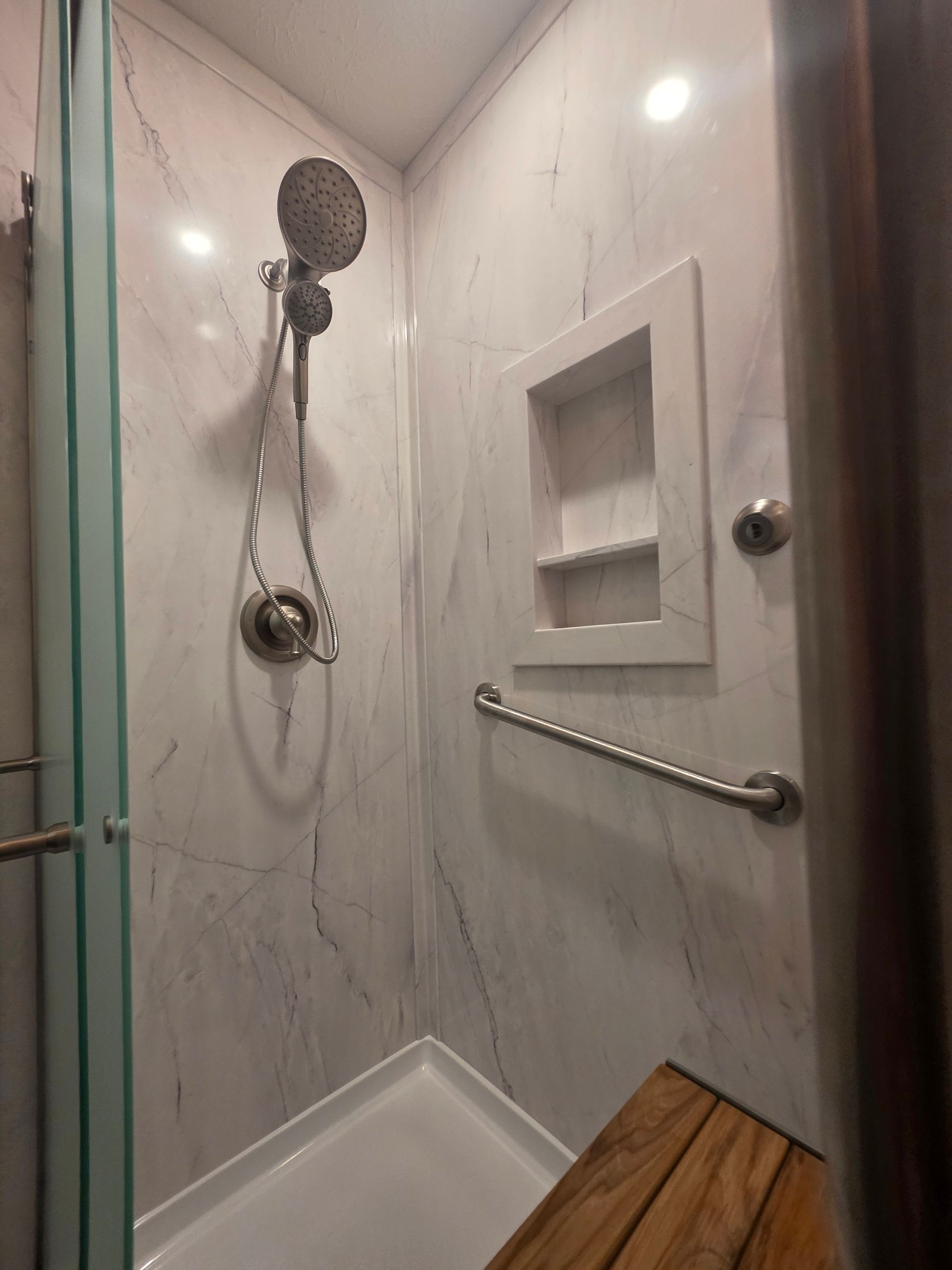 Accessible shower stall with grab bars and hand shower in a bathroom with striped wallpaper and a stack of towels.