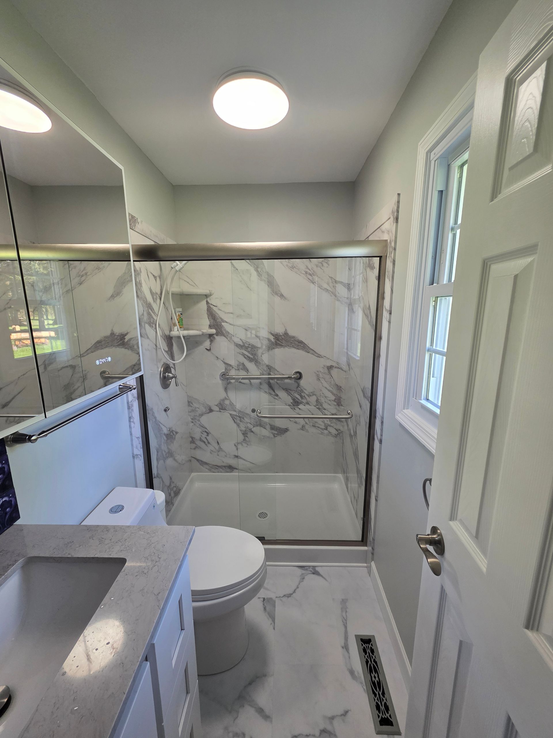 White bathroom with toilet, vanity, and mirror, against blue wall and gray floor.