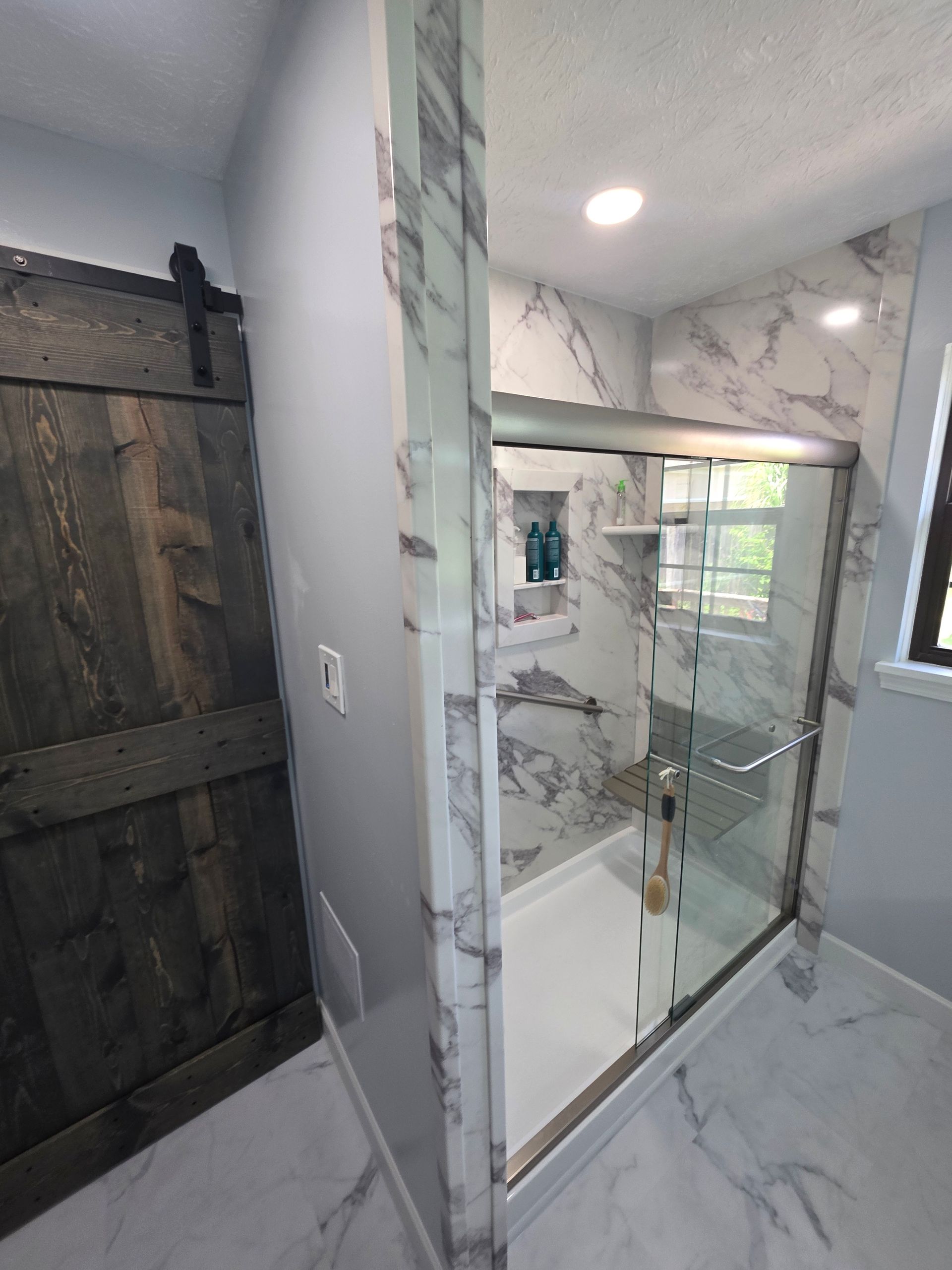 Accessible shower stall with grab bars and hand shower in a bathroom with striped wallpaper and a stack of towels.