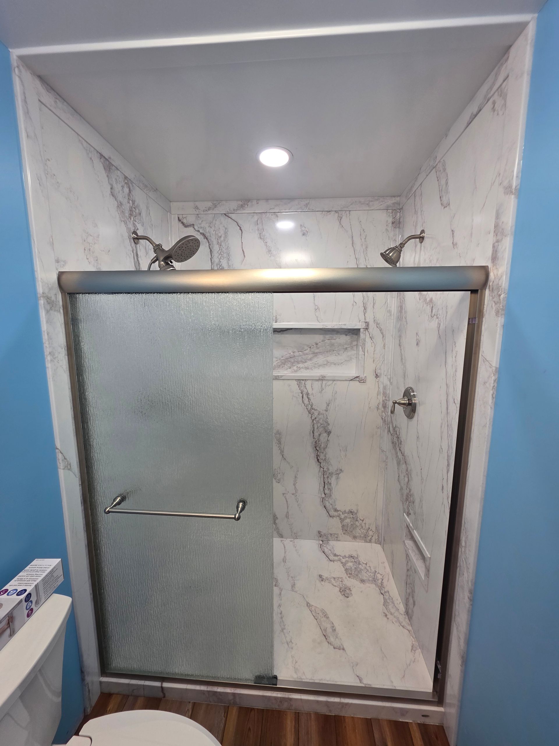 Small marble-tiled bathroom shower with glass door and overhead light