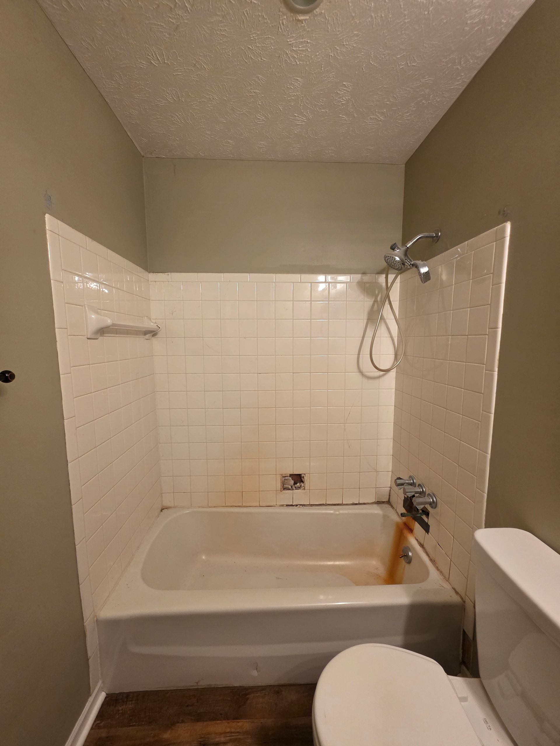 Small bathroom with a white bathtub, shower fixtures, and beige walls and tile.