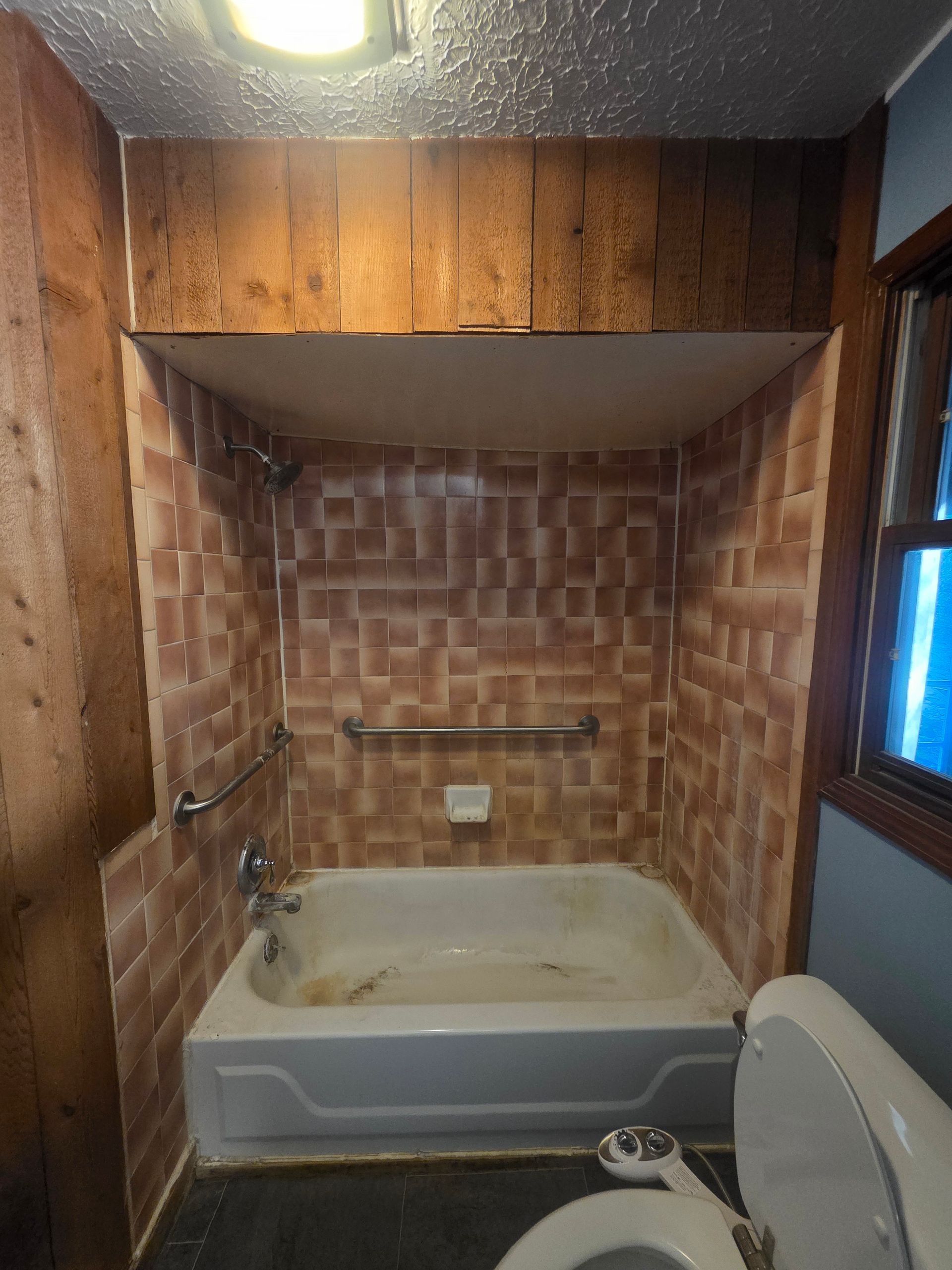 White bathroom with a tub, shower curtain rod, handheld showerhead, and patterned floor mat.