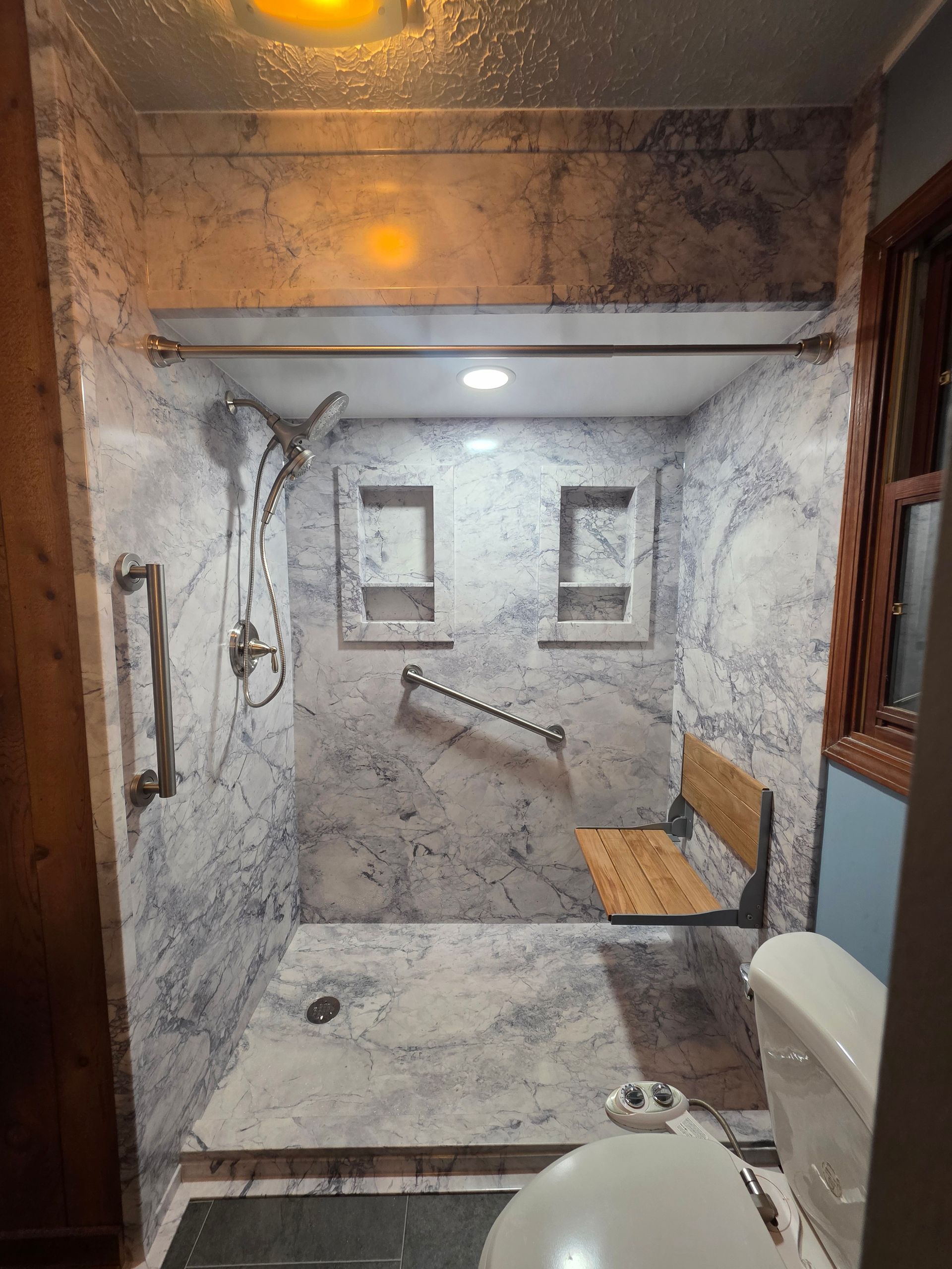 Accessible bathroom with roll-in shower, grab bars, shower seat, and handheld showerhead.