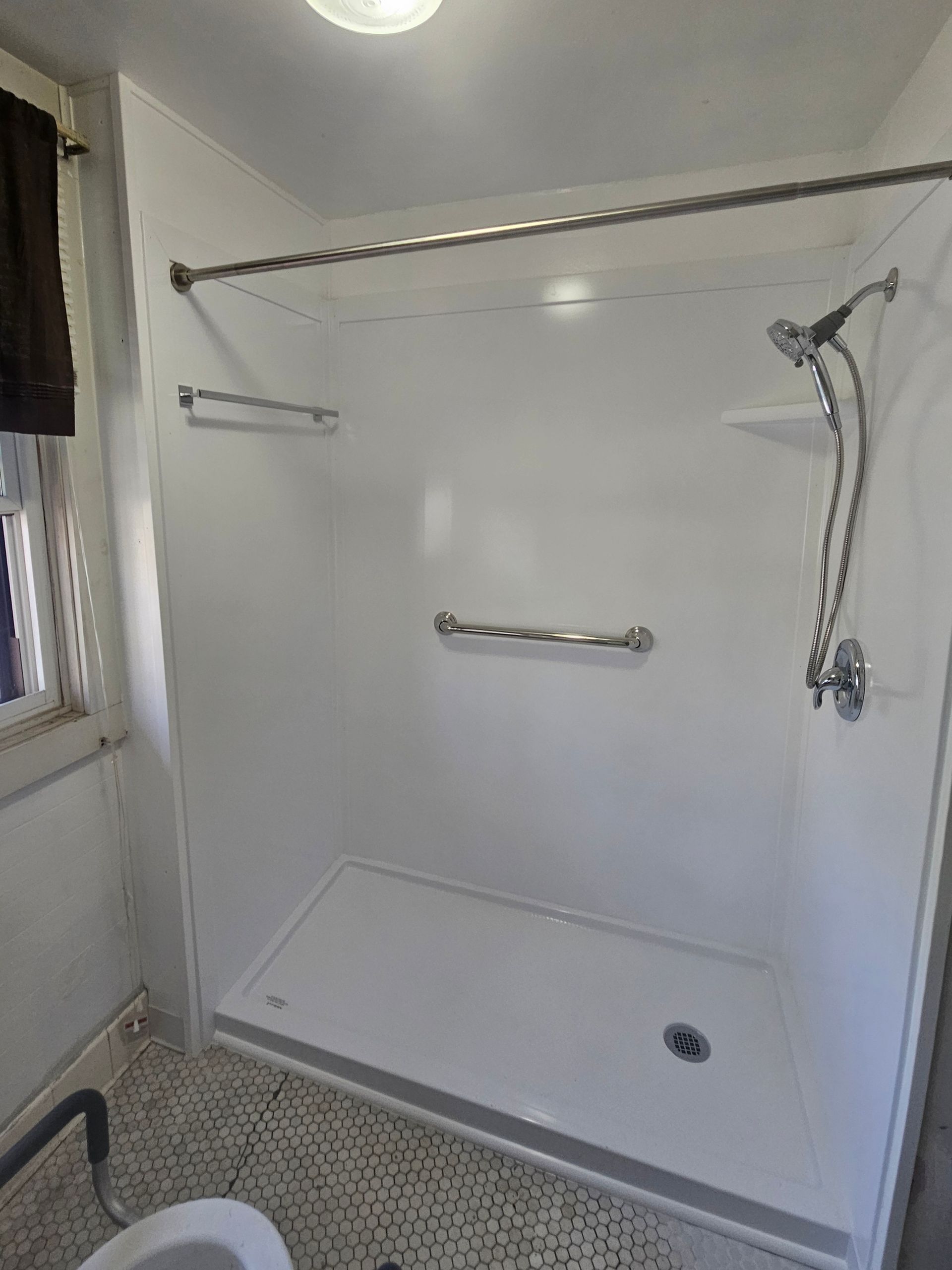 White shower stall with grab bars and a chrome shower head; next to a window.