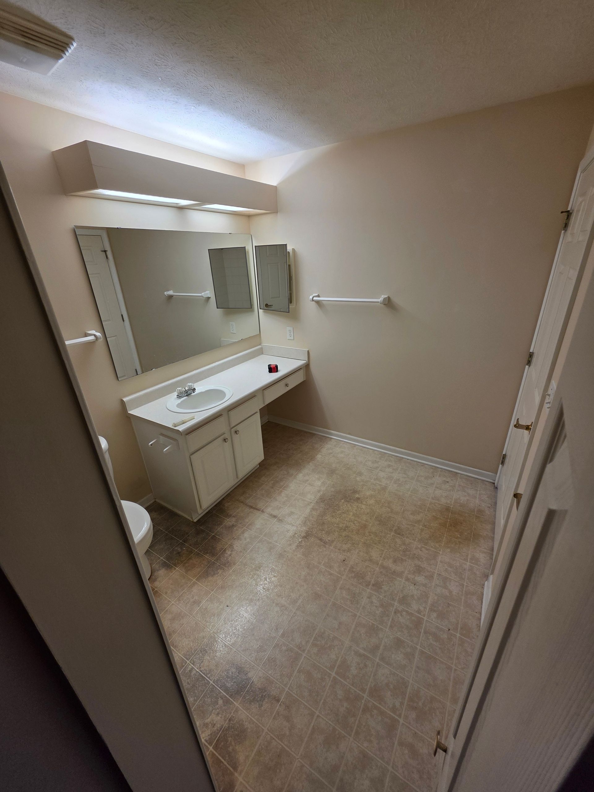 Bathroom with a white vanity, mirror, and stained floor.