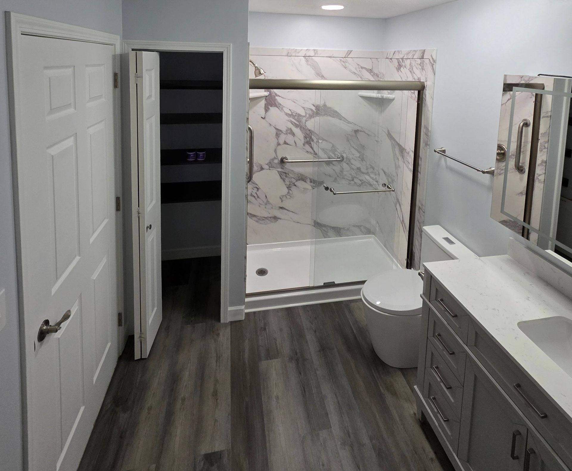 Modern bathroom with gray flooring, marble shower, white vanity, and closed white door.