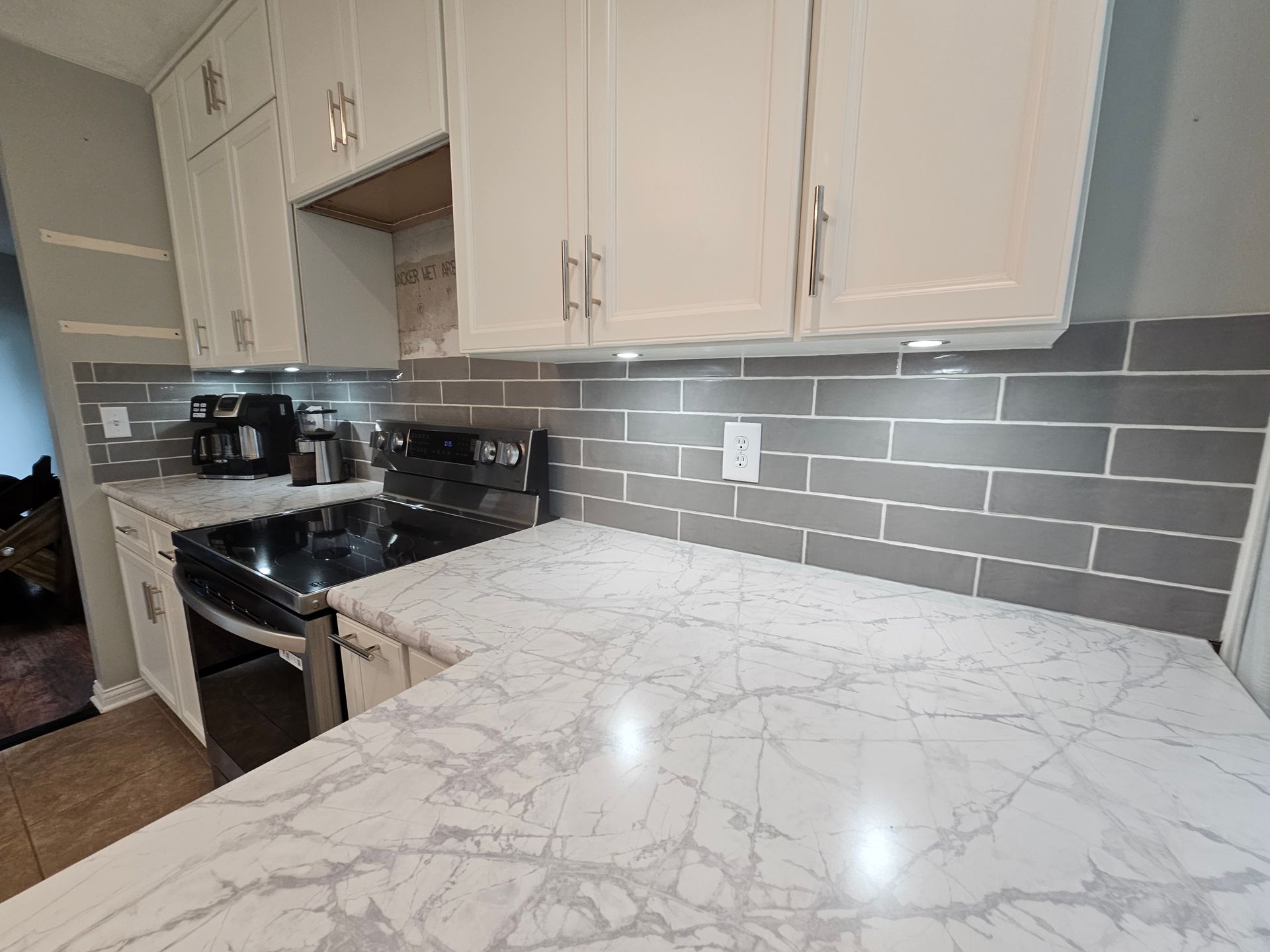 Kitchen with white cabinets, gray backsplash, and marble-patterned countertops.
