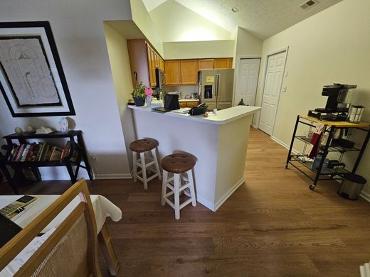 Kitchen with wood floor, stools at the counter, shelves with items, and a door.