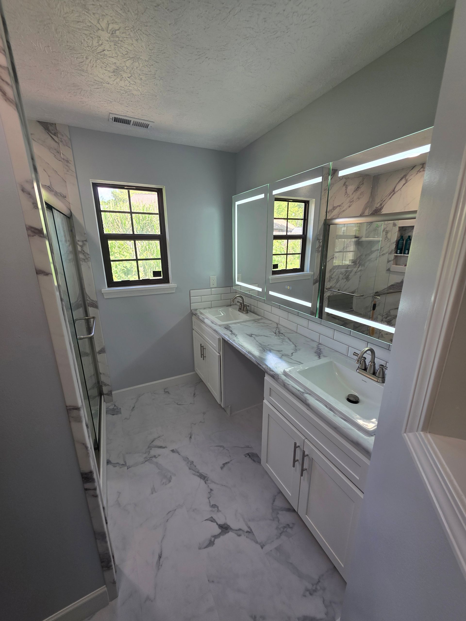 Narrow bathroom with double vanity, large mirror, white cabinets, and two small windows.