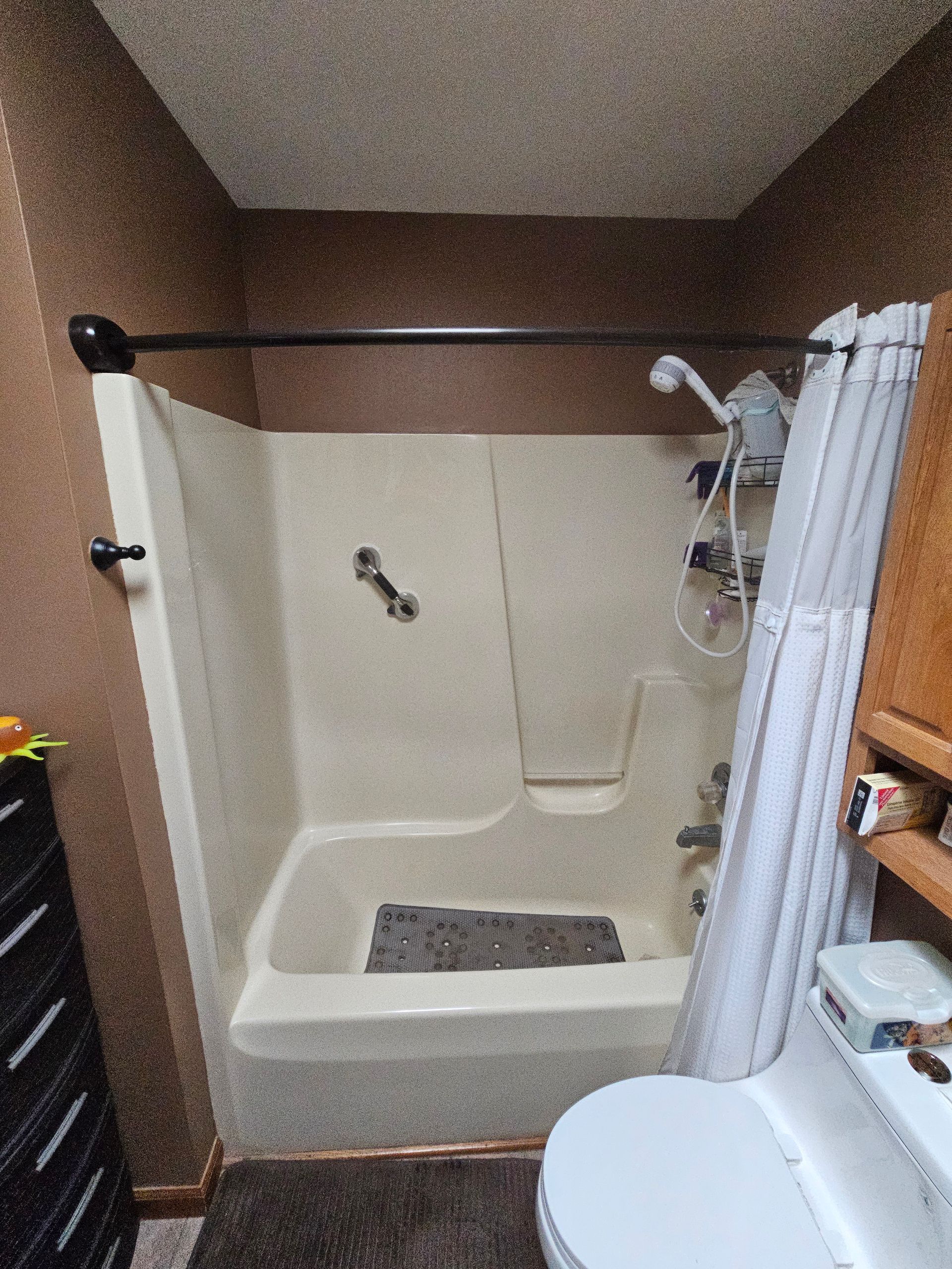 Tan and brown bathroom with a shower-tub combo, shower curtain, toilet, and dark brown walls.