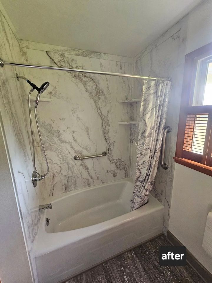 Bathroom with white tub, marble-patterned walls, shower curtain, and grab bars.