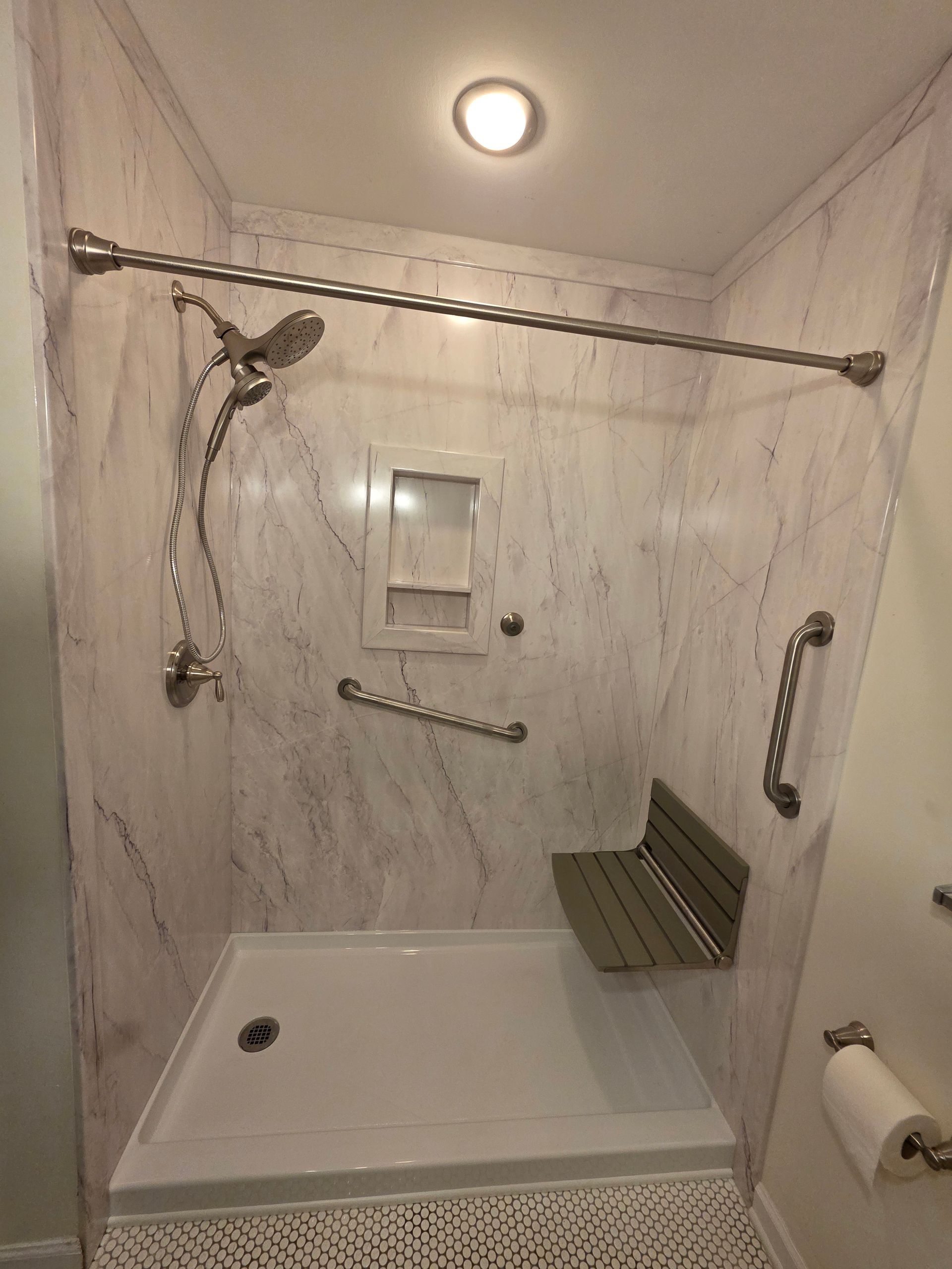 Accessible bathroom with roll-in shower, grab bars, shower seat, and handheld showerhead.